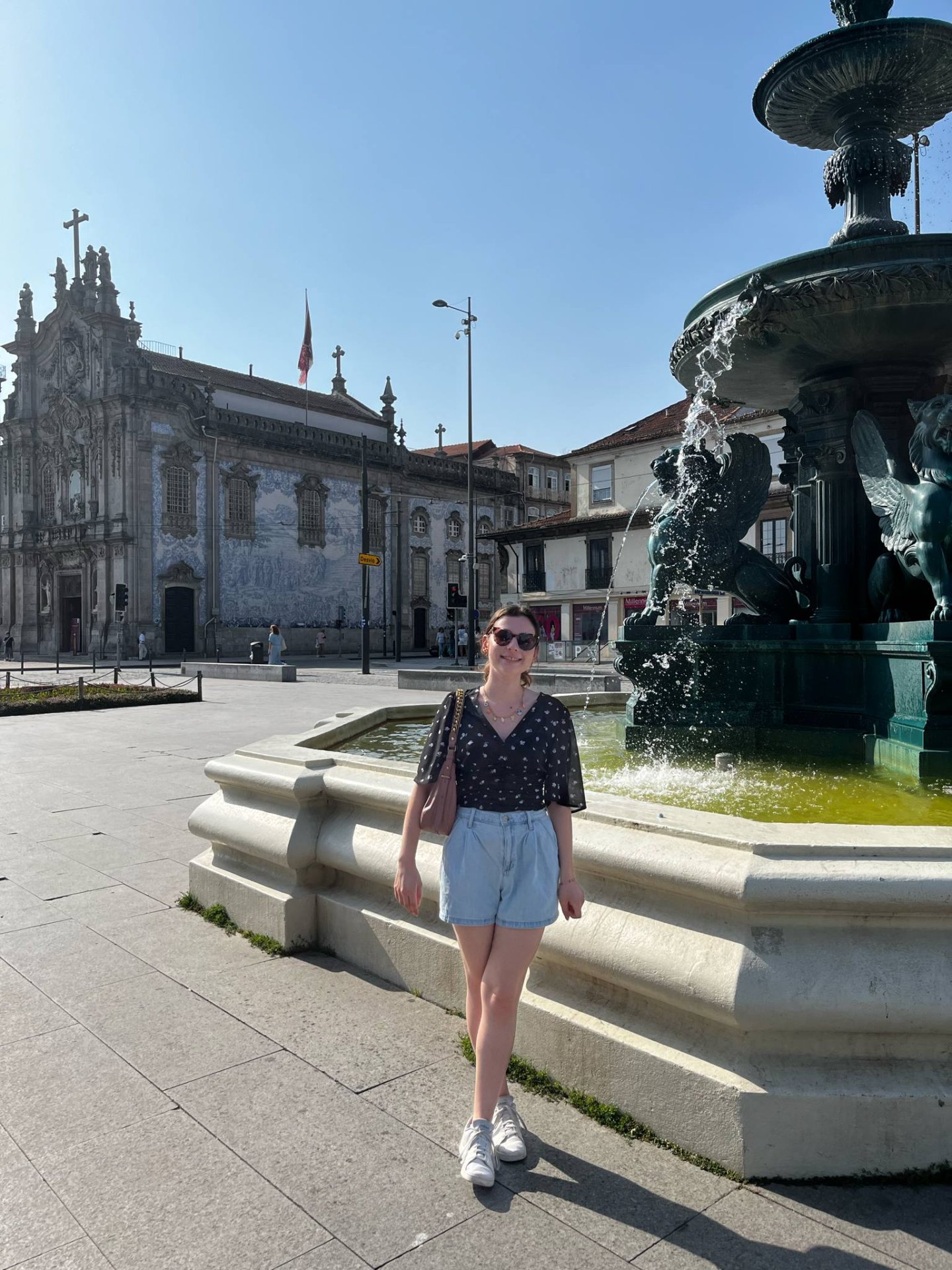 Jeune femme posant devant une fontaine et une église historique en extérieur